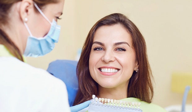 A dentist using a shade guide and a female patient smiling