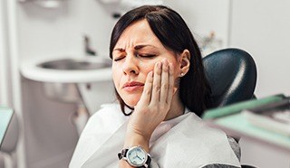 Woman in dental chair holding cheek