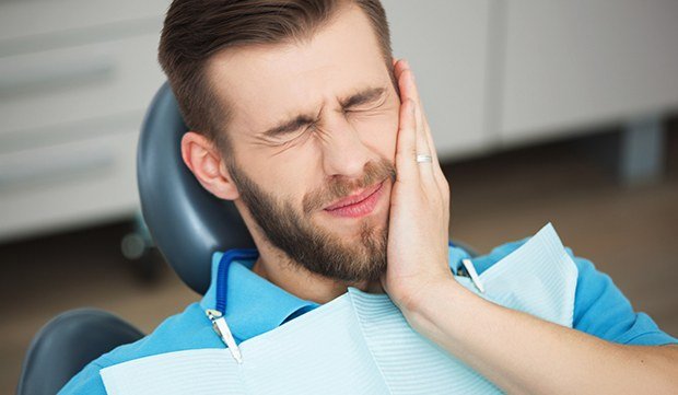 Man in dental chair holding cheek